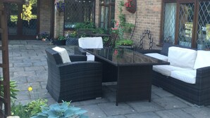 Un'area patio con mobili in vimini, una pianta in vaso e un edificio in mattoni con finestre.