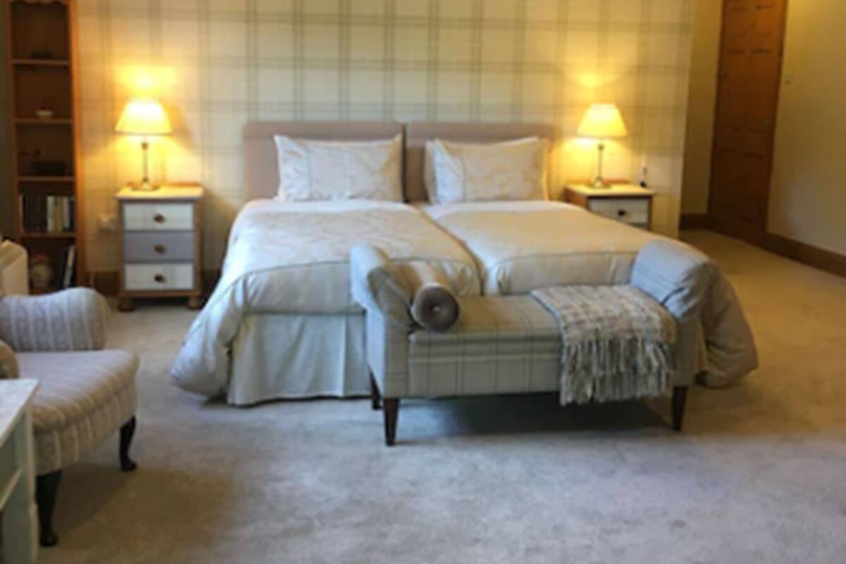 A bedroom with a double bed, two bedside tables with lamps, a chair, a bookshelf, and a door.