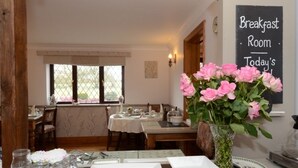 Una sala colazione con una lavagna, un vaso di fiori rosa e un tavolo imbandito con piatti e bicchieri.