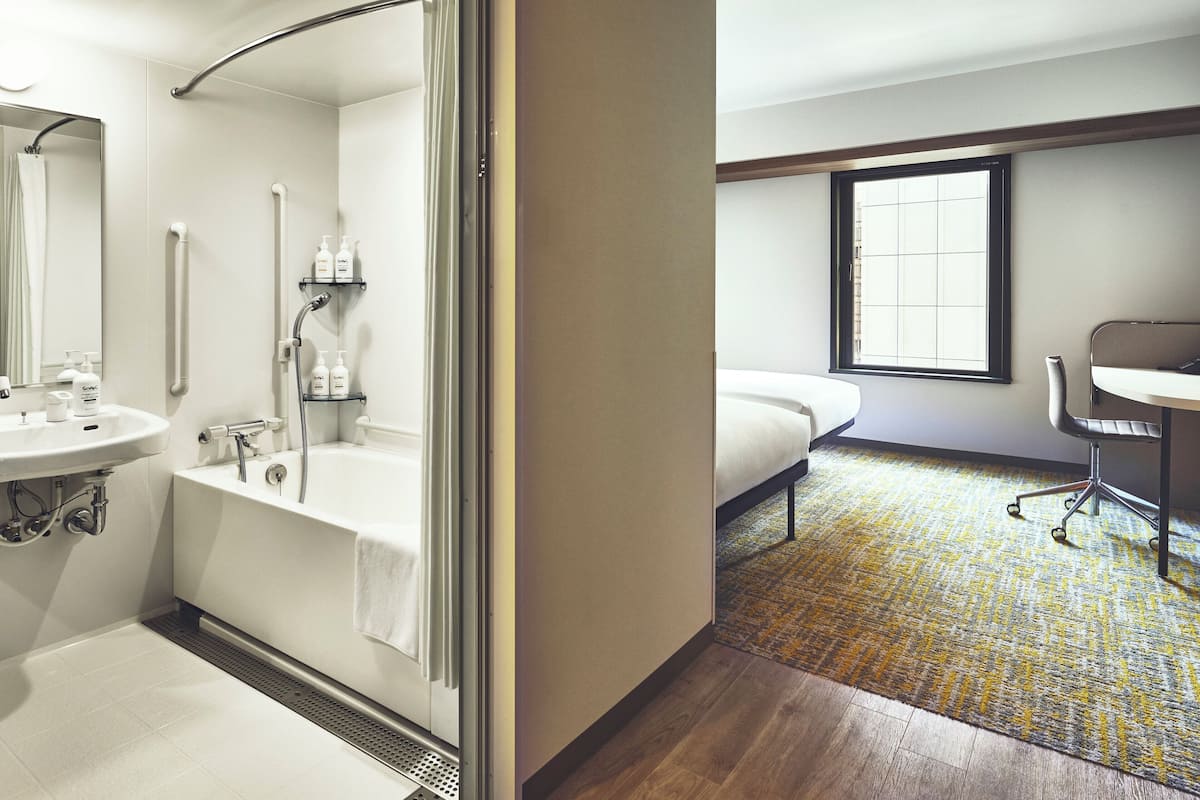 A modern bathroom with a bathtub, sink, and shower. There is a bed with a window and a desk with a chair.