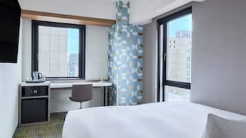 Habitació d'hotel amb un llit, una taula de treball amb una cadira, microones i una finestra que ofereix vistes a la ciutat.
