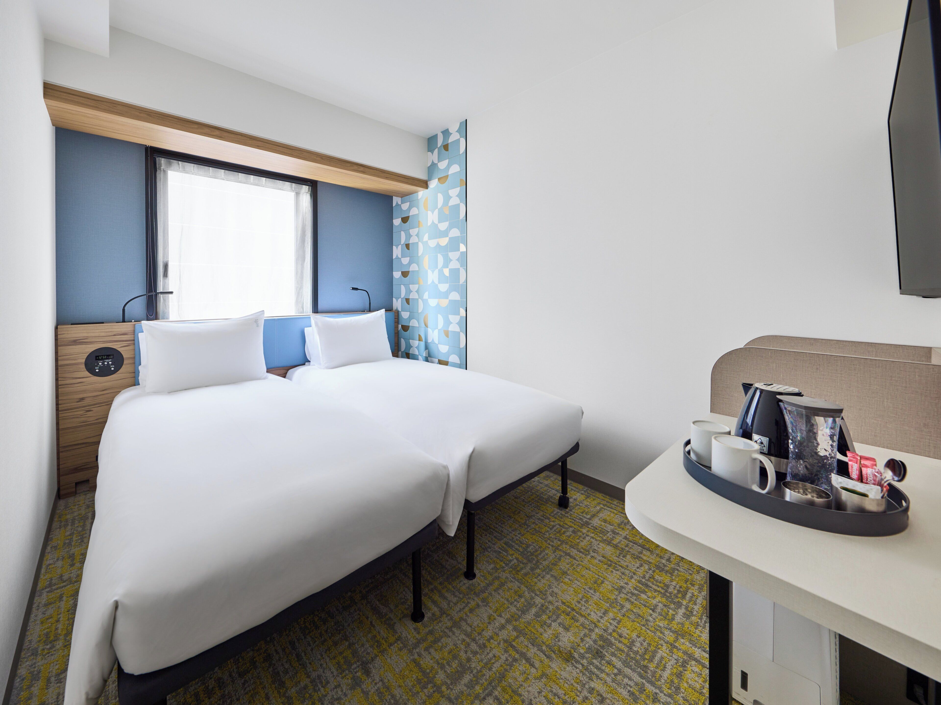 Quarto de hotel com uma cama, mesa de cabeceira e televisão.