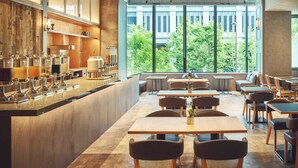Una cafetería moderna con una barra larga, diversas opciones de asientos y amplios ventanales con vistas al exterior.