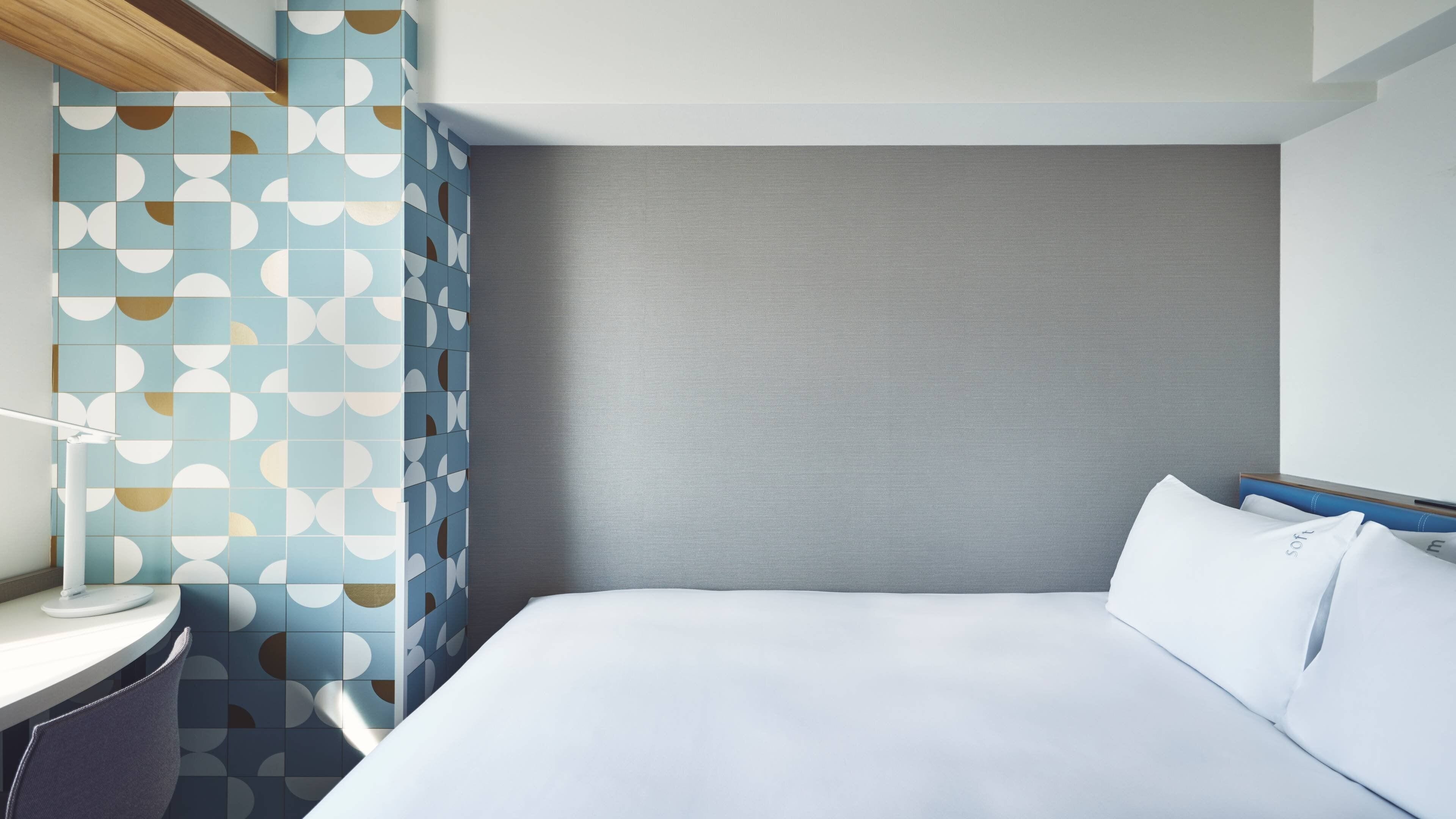 A modern hotel room with a large bed, a bedside table, and a wall with a geometric tile pattern.