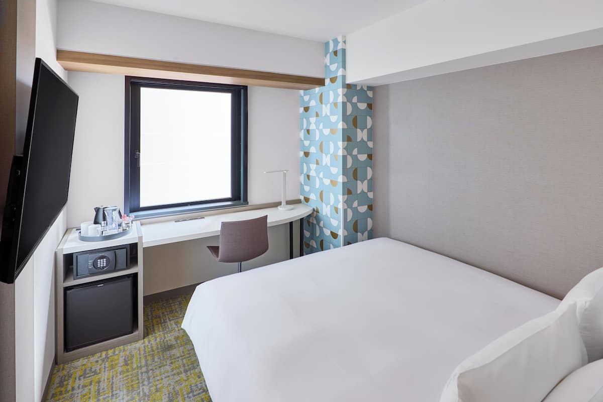 A hotel room with a bed, a desk with a chair, a television, and a window.
