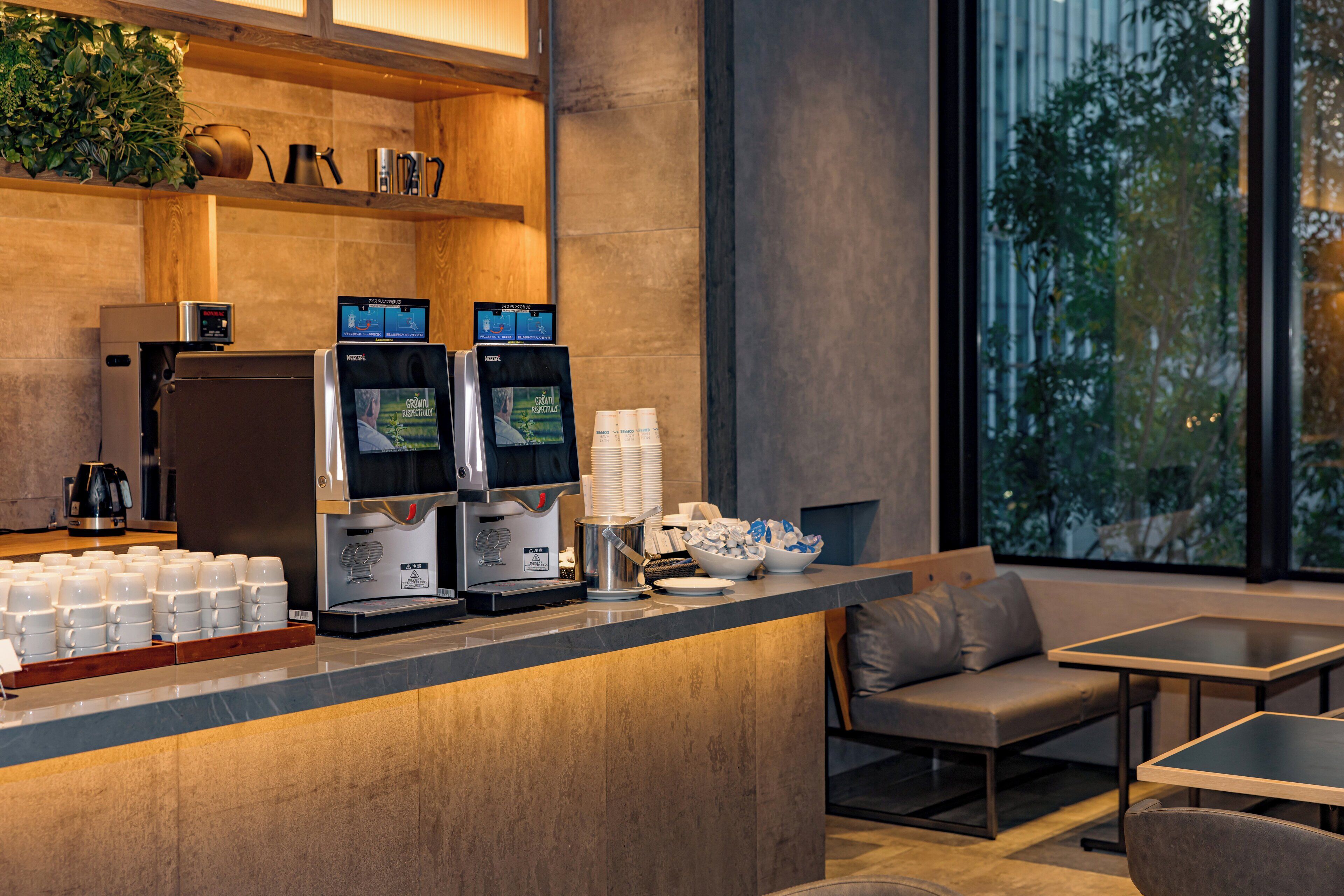 A modern coffee station with espresso machines, a coffee press, and a seating area with a sofa and tables.