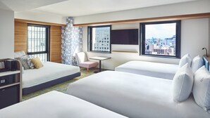 Habitación de hotel con dos camas, un escritorio, una silla, un televisor y ventanas amplias con vista a la ciudad.