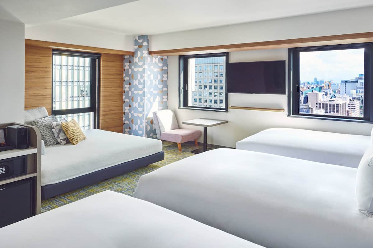 A hotel room with two beds, a desk, a chair, a TV, and large windows with a city view.