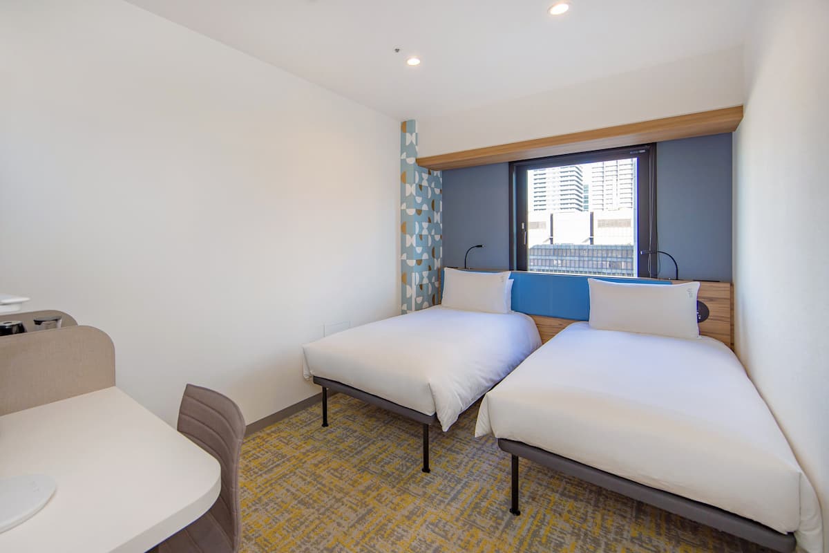 A hotel room with two beds, a small table, and a chair.