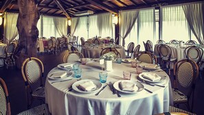 Comedor con mesas redondas dispuestas para una comida, rodeado de sillas de mimbre, bajo un techo de madera.