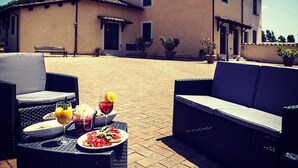 Un área de comedor al aire libre con mobiliario de mimbre y una mesa servida con platos, vasos y bebidas.