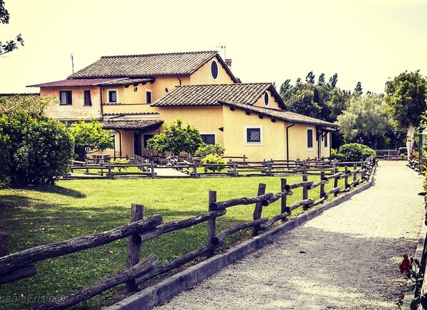 A two-story building with a tiled roof, surrounded by a gravel path and a wooden fence. - Relais Il Casale (Rome)