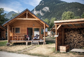 Une cabane en bois avec un porche, un espace abrité doté d’un foyer, et une vue sur les montagnes en toile de fond.