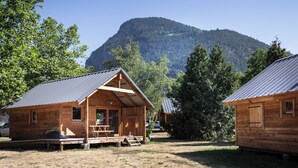 Una cabaña de madera con un porche y una mesa de comedor, rodeada de árboles y una montaña al fondo.