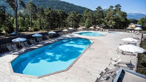 Zona de piscina con dos piscinas, sillas de descanso, sombrillas y una terraza de madera.
