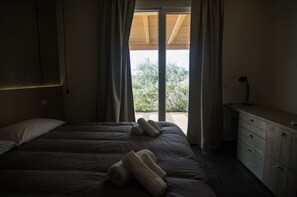 A bedroom with a large bed, a wooden headboard, a nightstand, and a view of greenery outside.
