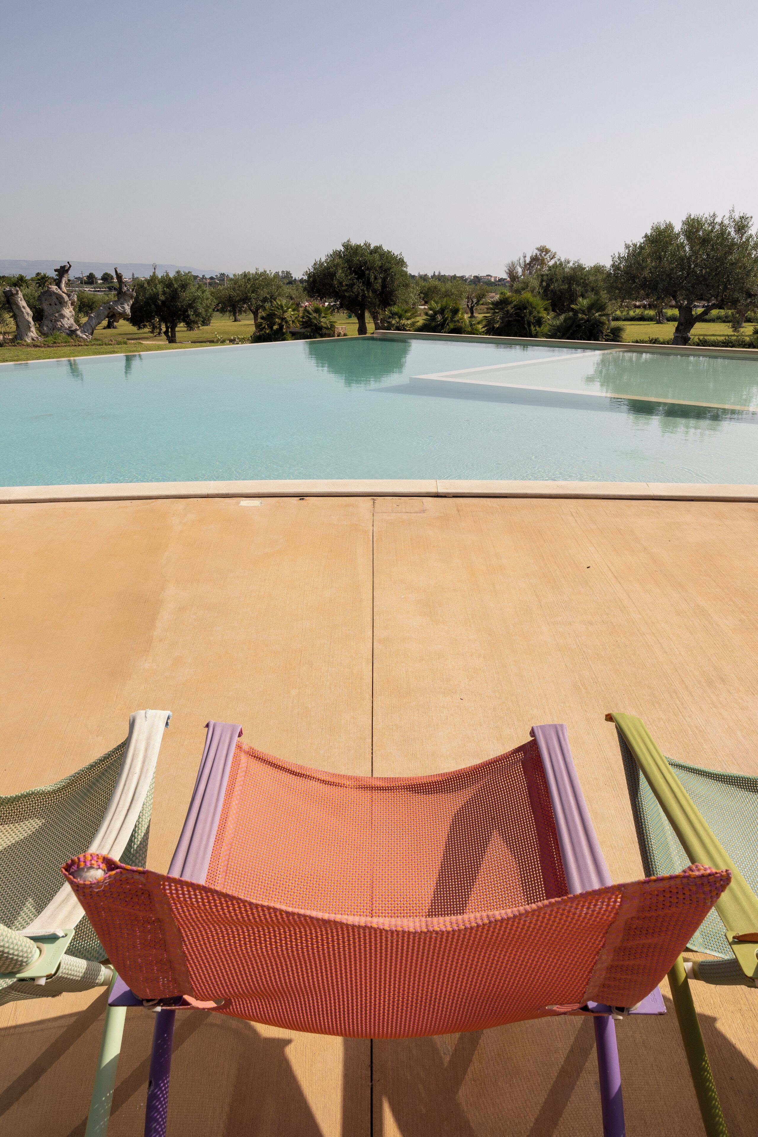 Una silla hamaca con vistas a una piscina, árboles y un cielo despejado.