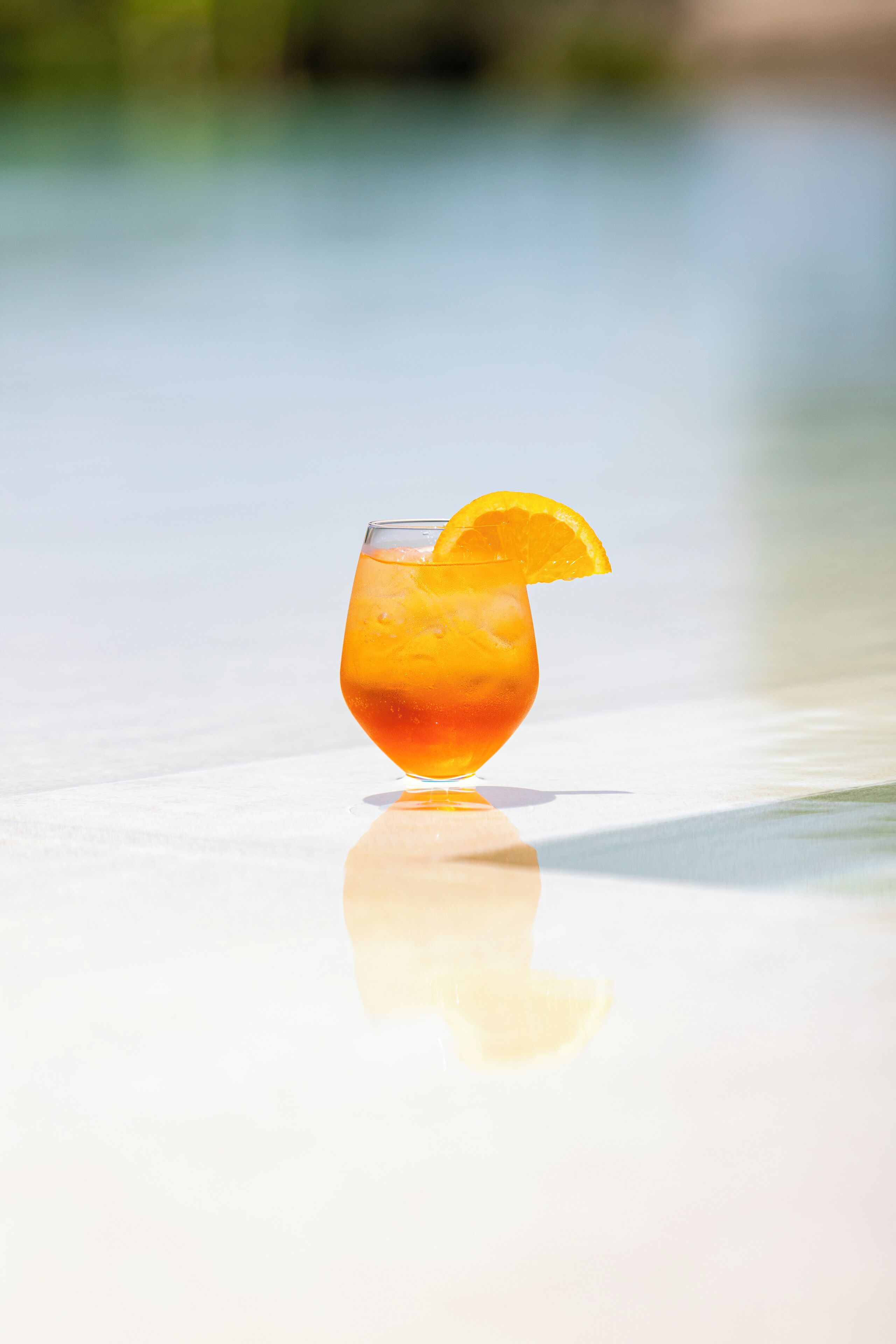 Een glas oranje drank met een sinaasappelschijfje op de rand, geplaatst op een reflecterend oppervlak.