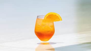 Een glas oranje drank met een sinaasappelschijfje op de rand, geplaatst op een reflecterend oppervlak.