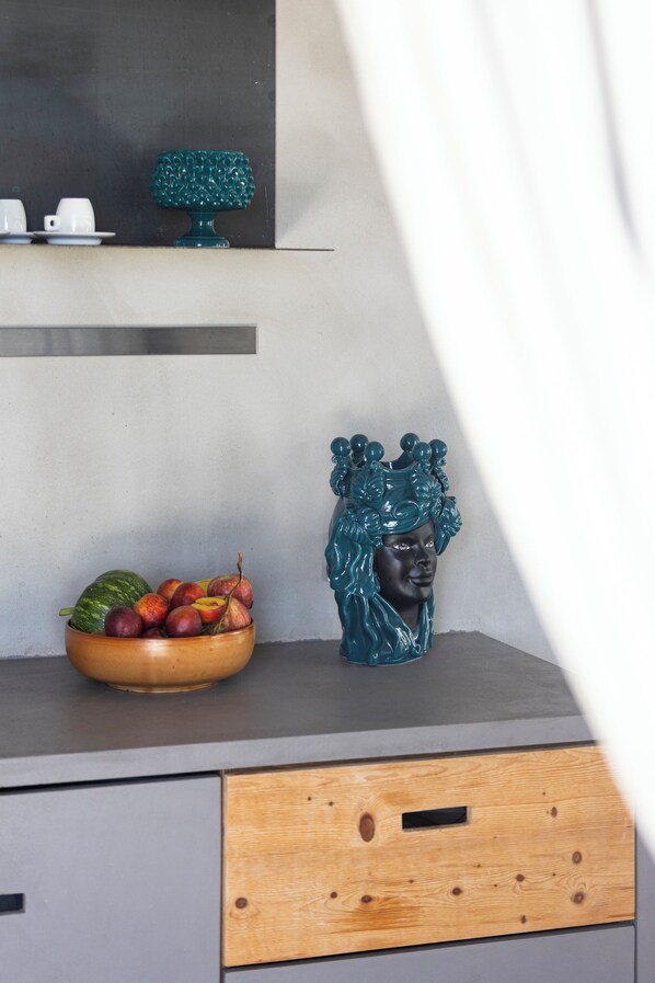 A kitchen counter with a fruit bowl, a teal decorative item, and a bust sculpture.