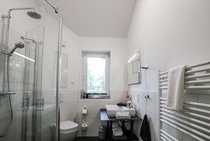 A modern bathroom with a glass shower enclosure, a toilet, a sink with a mirror above, and a towel rack.