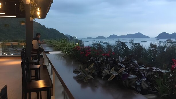 Un restaurante con terraza al aire libre, vistas a un cuerpo de agua y colinas.