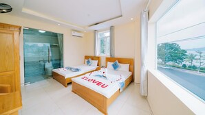 Habitación de hotel con dos camas, cabina de ducha de vidrio, armario de madera y un amplio ventanal con vistas a la ciudad.