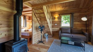A cozy wooden cabin interior with a wood-burning stove, a sofa, and a fan. - Huttopia Font Romeu (Font-Romeu-Odeillo-Via)