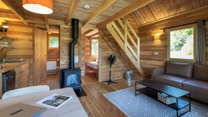 A cozy cabin interior with a wooden interior, a sofa, a dining table, and a fireplace. - Huttopia Font Romeu (Font-Romeu-Odeillo-Via)