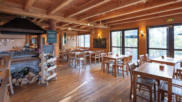 A wooden interior with tables and chairs, a fireplace, and large windows. - Huttopia Font Romeu (Font-Romeu-Odeillo-Via)