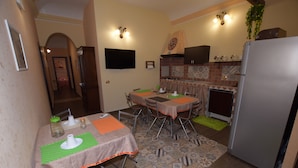 A compact kitchen with a refrigerator, a dining table with chairs, and a TV mounted on the wall. - B&B Empedocle (Porto Empedocle)