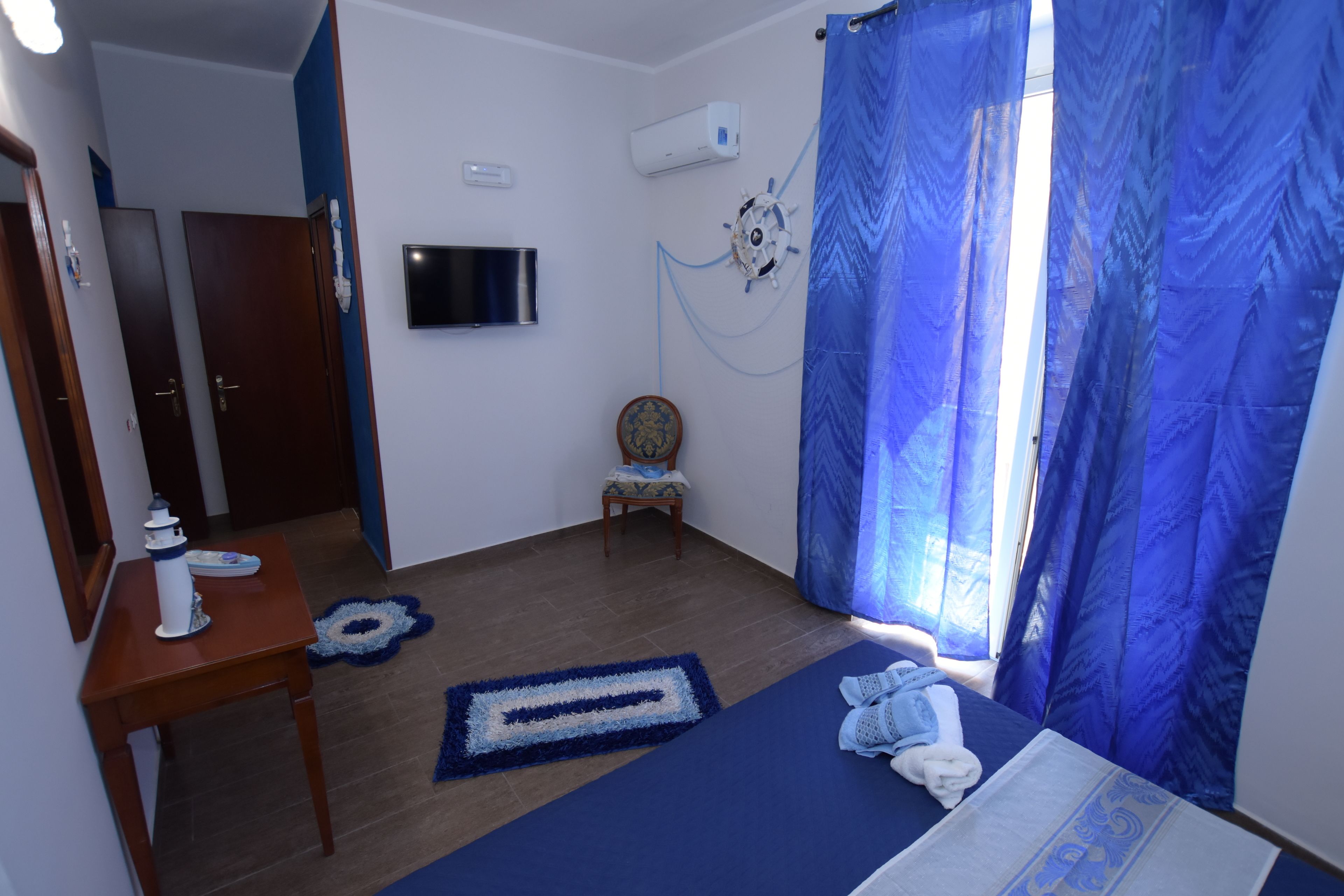 Une chambre à coucher avec un lit, un bureau, une chaise, un téléviseur et une fenêtre avec des rideaux bleus.