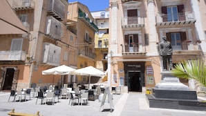A square with outdoor seating, a statue, and multi-story buildings with balconies. - B&B Empedocle (Porto Empedocle)