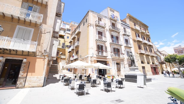 A square with outdoor seating, a statue, and multi-story buildings with balconies. - B&B Empedocle (Porto Empedocle)