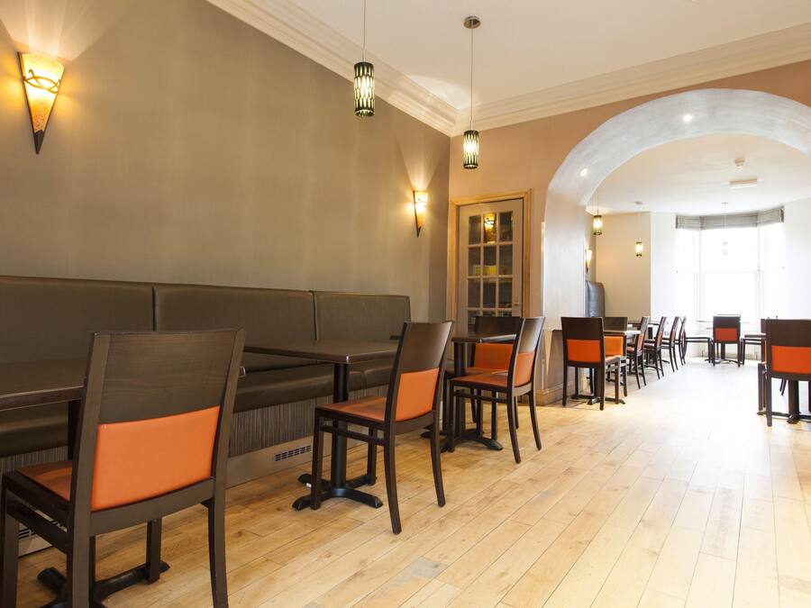 A restaurant with wooden tables and chairs, a long bench, and wall sconces.