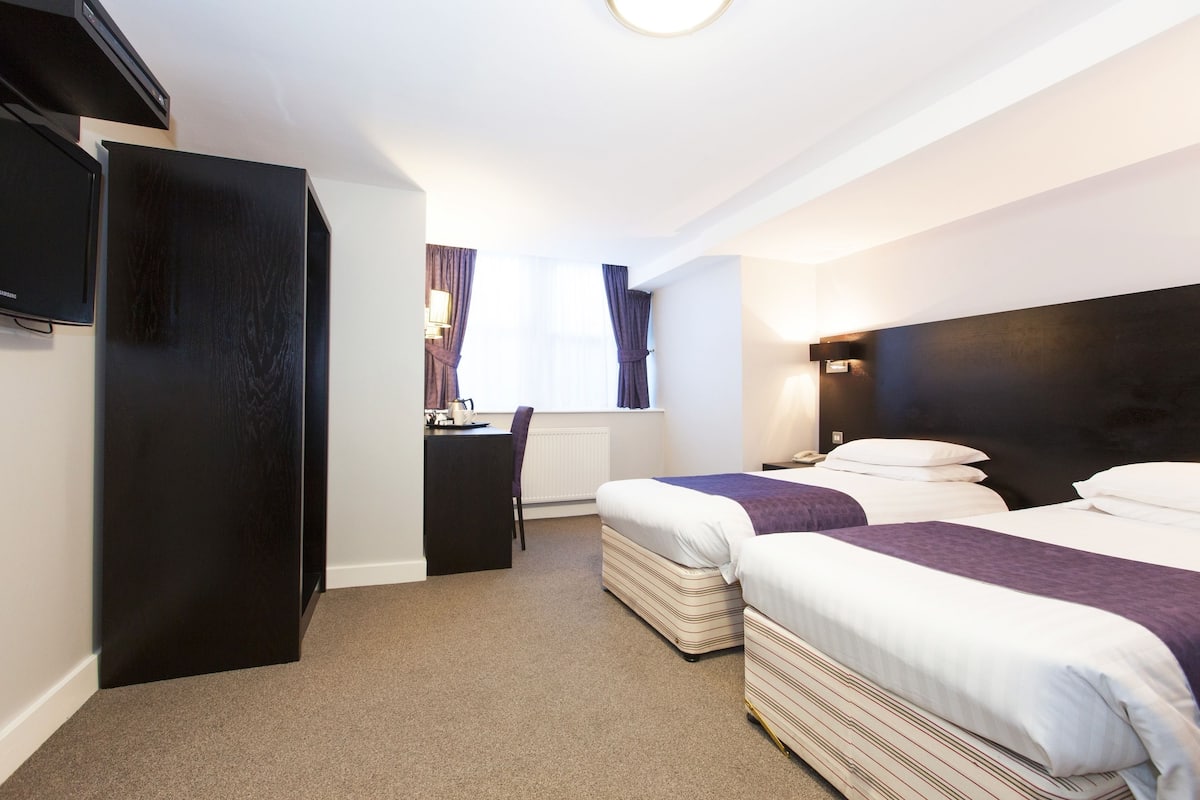 A hotel room with two beds, a desk, a television, and a window with curtains.