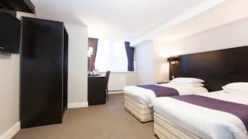 A hotel room with two beds, a desk, a television, and a window with curtains.