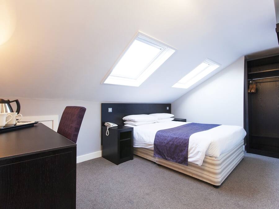 A hotel room with a bed, a desk, a chair, and two skylights.
