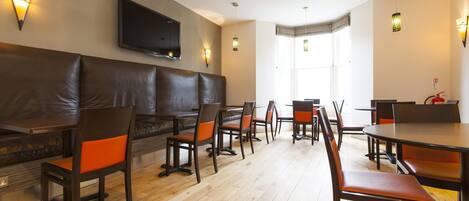 A restaurant with wooden flooring, leather booths, and orange chairs.