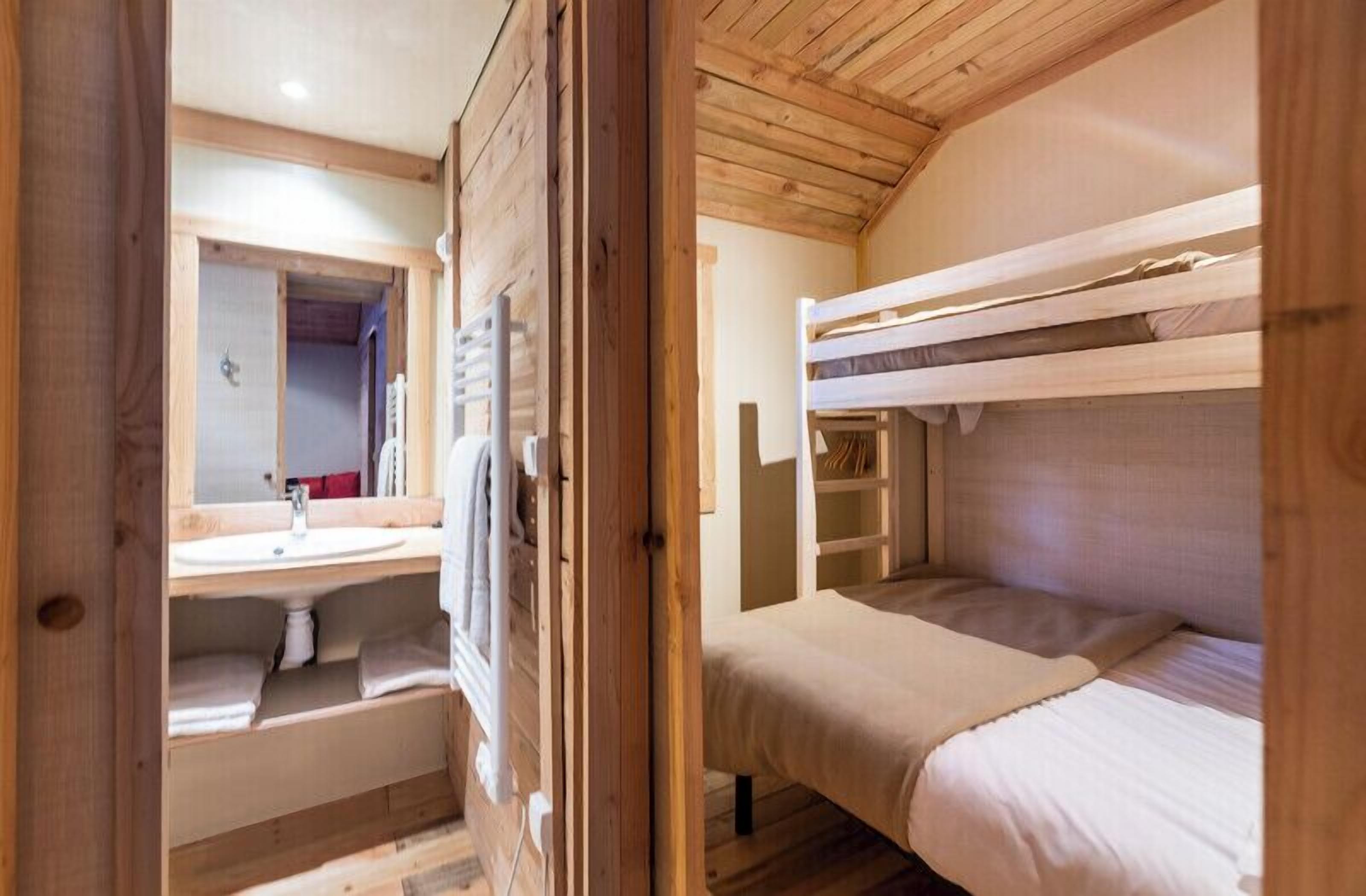 Eine Holzhütte mit einem Etagenbett, einem Badezimmer mit Waschbecken und Spiegel sowie einer kleinen Ablagefläche.