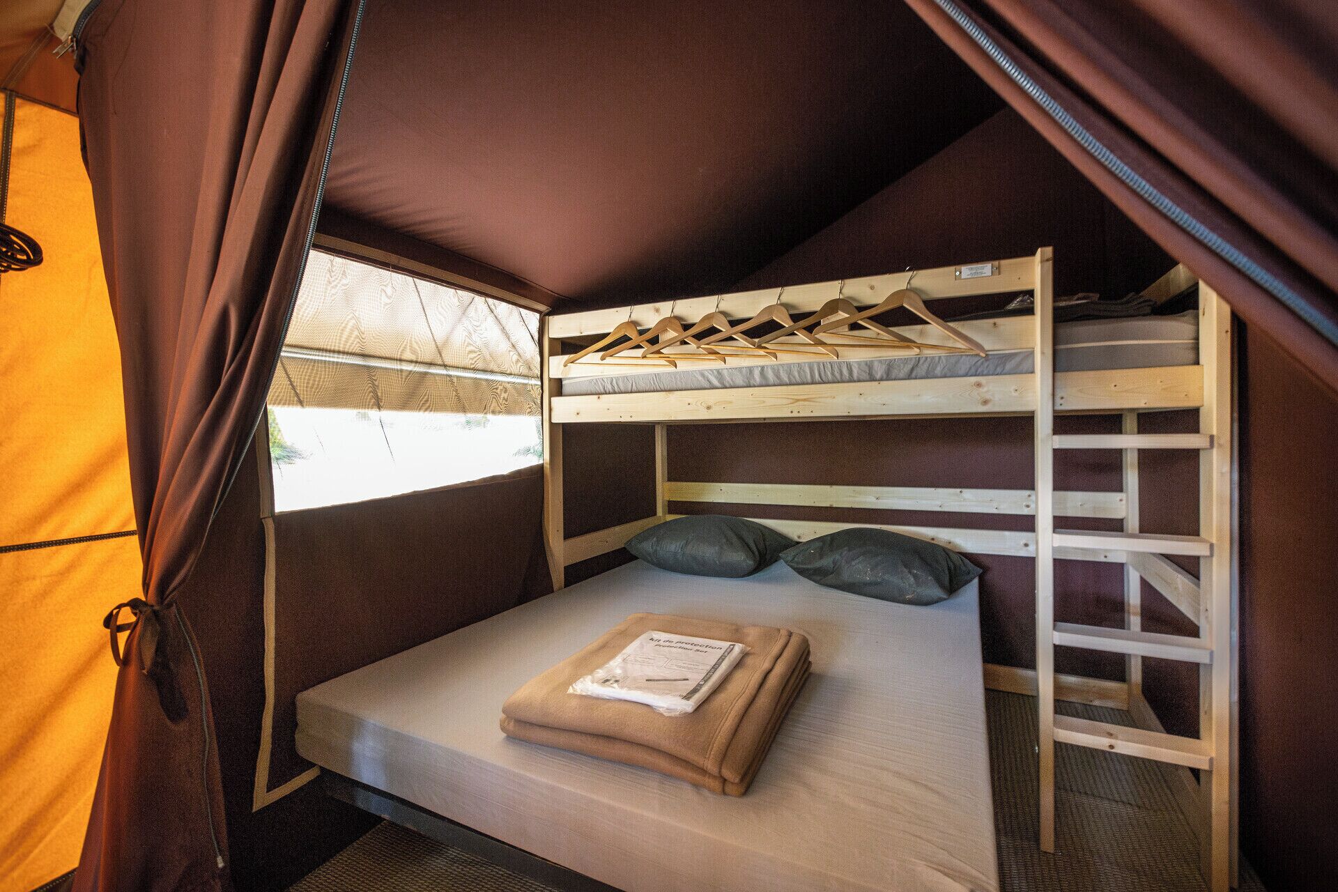 Un lit superposé avec un matelas et des oreillers, une fenêtre avec des rideaux et un porte-vêtements suspendu.