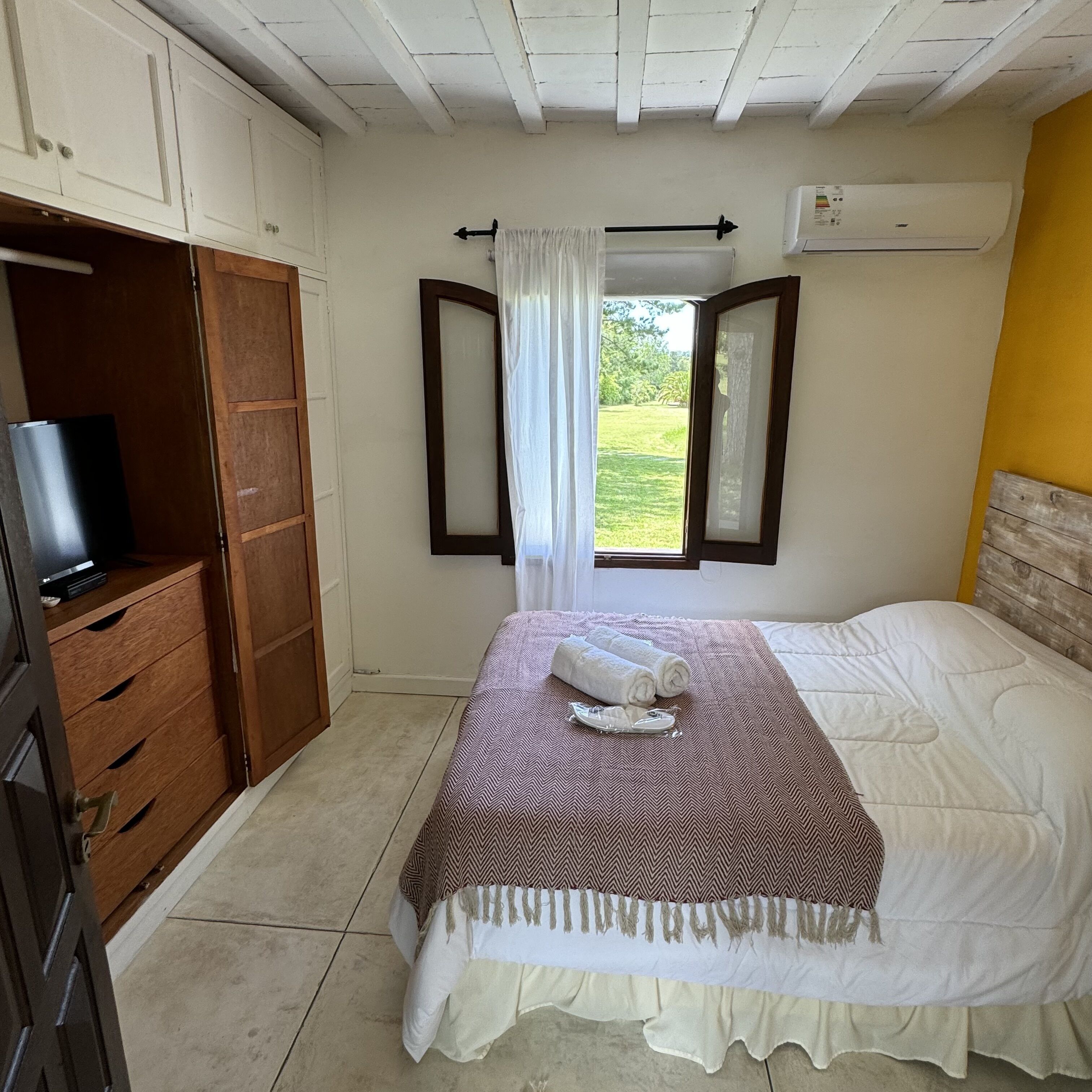 Un dormitorio con cama, televisión, armario y ventana con cortinas.
