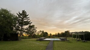Una terraza de madera que conduce a una piscina con un porche y mesas de picnic en un patio trasero.