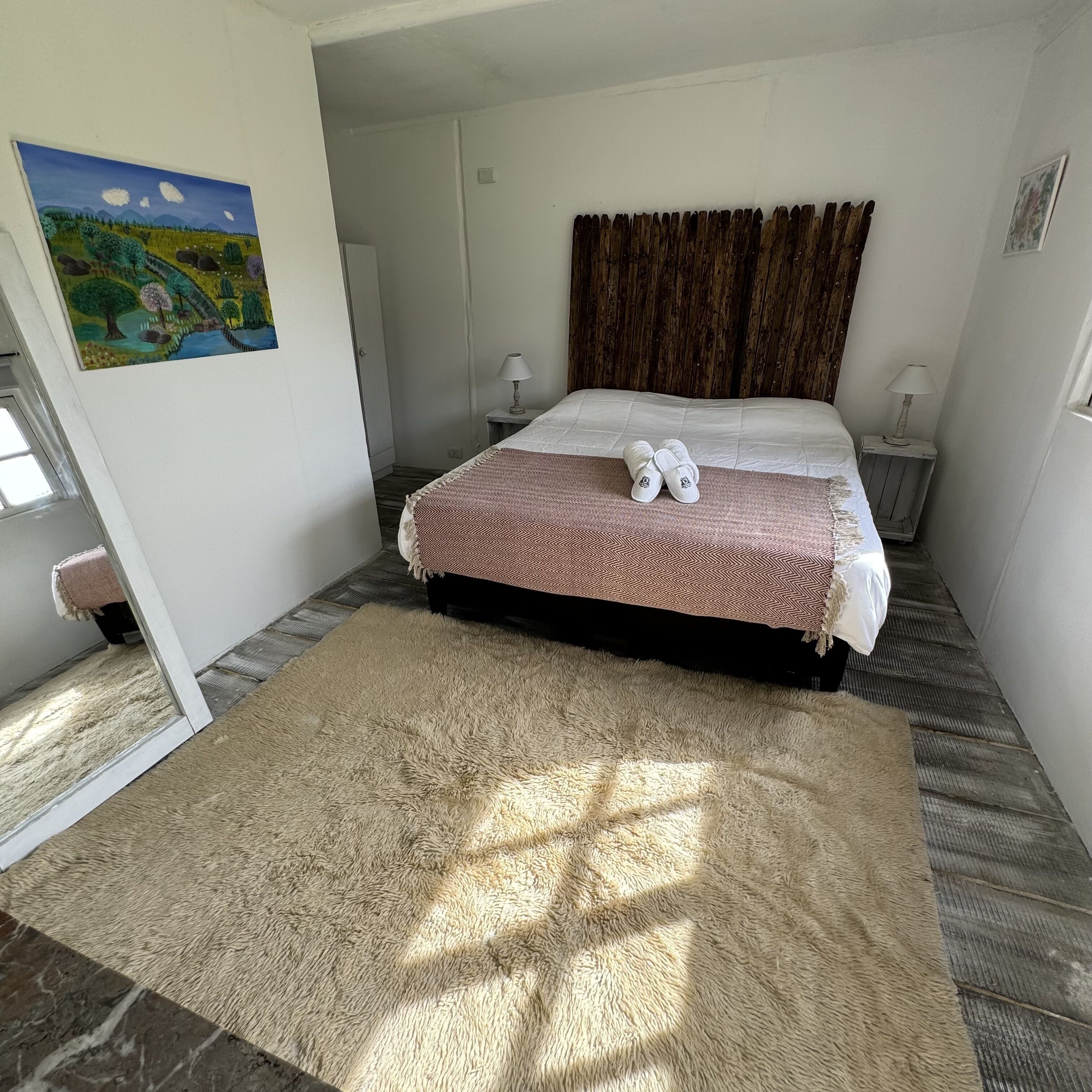 Ein Schlafzimmer mit Bett, Teppich, Gemälde und hölzernem Kopfteil.