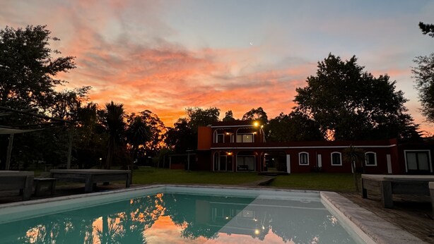 Una piscina con vistas a un atardecer, un edificio rojo y árboles circundantes.