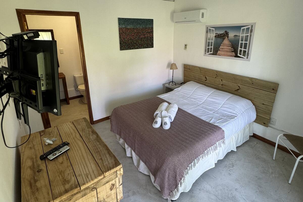 Quarto com cama, cómoda de madeira, televisão e pintura na parede.