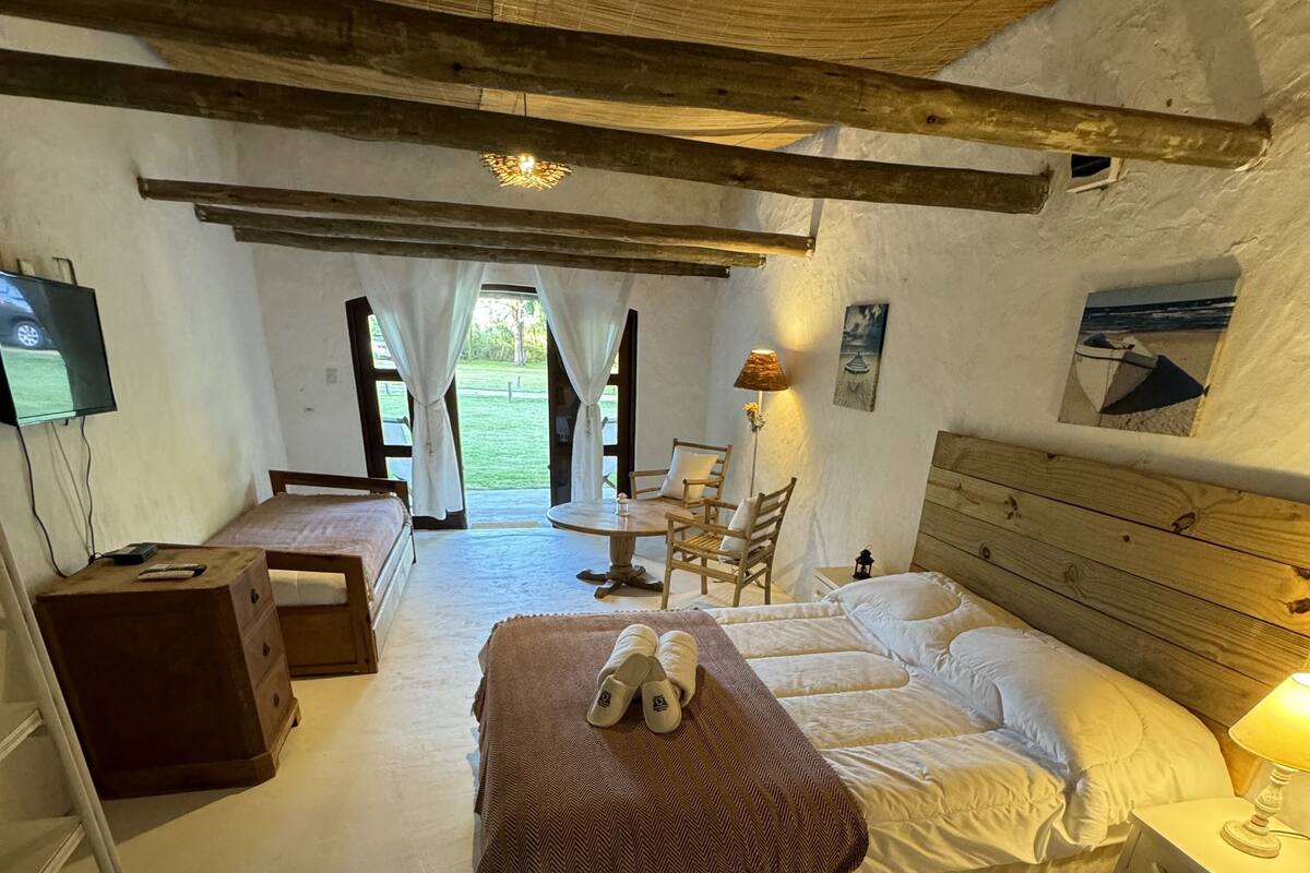 Quarto com cama, mesas de cabeceira, uma cadeira, luminária e televisão.