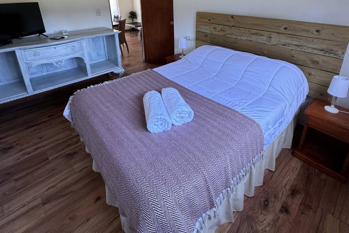Quarto com uma cama, uma TV em uma cômoda e uma cabeceira de madeira.