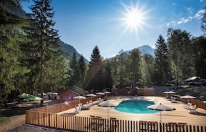 Un espace piscine doté de chaises longues et de parasols, entouré d’arbres et de montagnes.