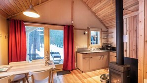 En mysig stuga med träinredning, en matplats med bord och stolar, ett kök med spis och utsikt över omgivningen.